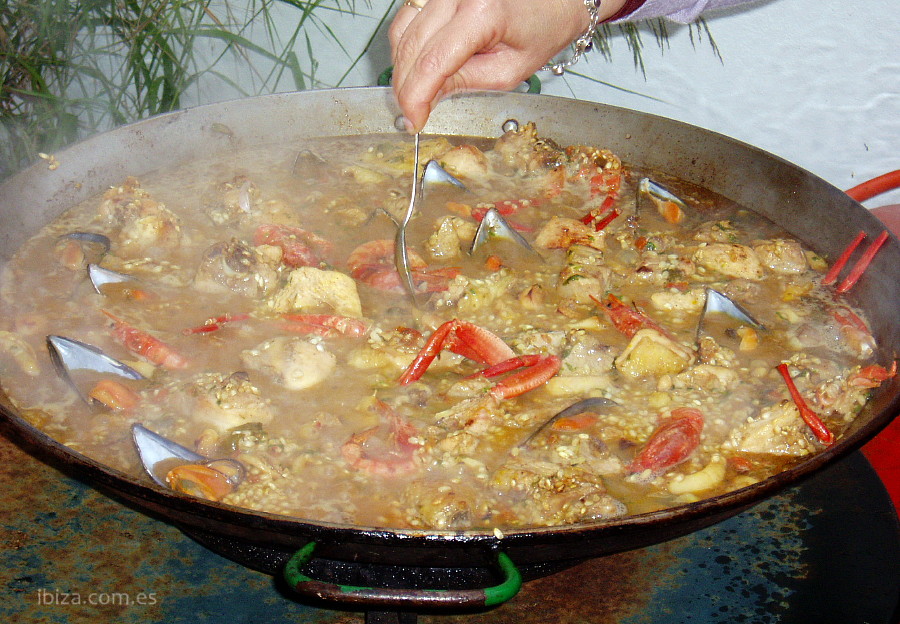 Paella mixta de pescado y carne hecha al fuego, recibiendo los útimos toques de salazón
